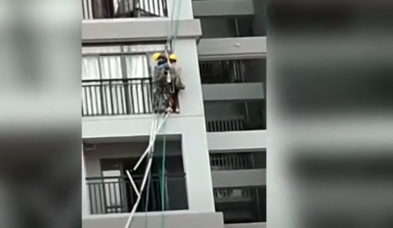 Të lidhur me litarë, dy punëtorët lëkunden nga erërat e forta në qindra metra lartësi