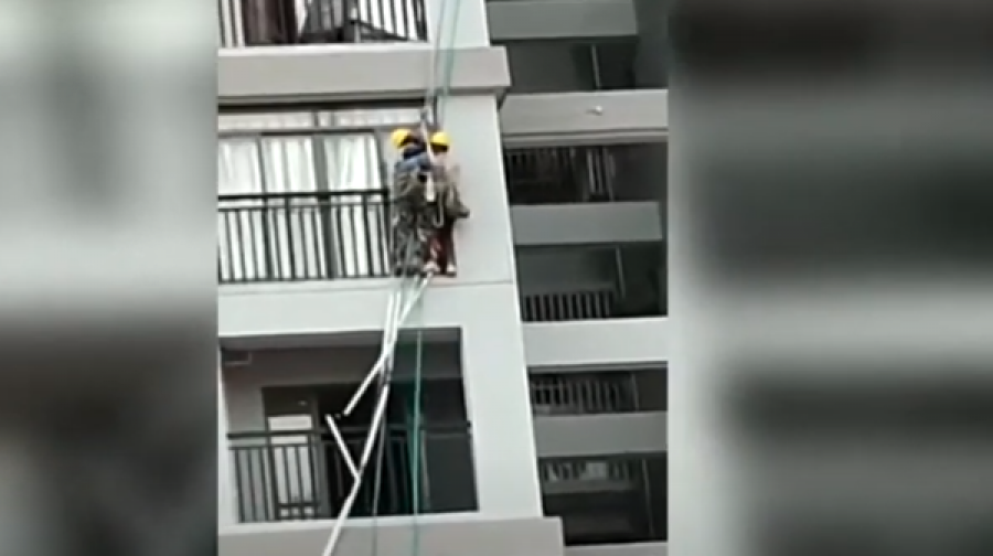 Të lidhur me litarë, dy punëtorët lëkunden nga erërat e forta në qindra metra lartësi